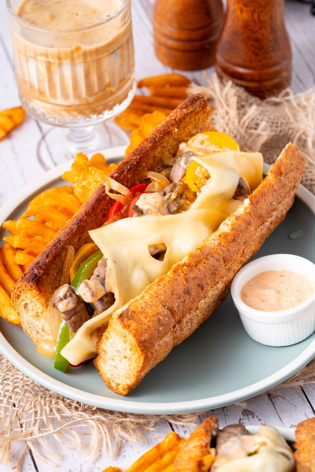 A cheesy sandwich with peppers and meat, served with waffle fries, dipping sauce, and a cold drink.