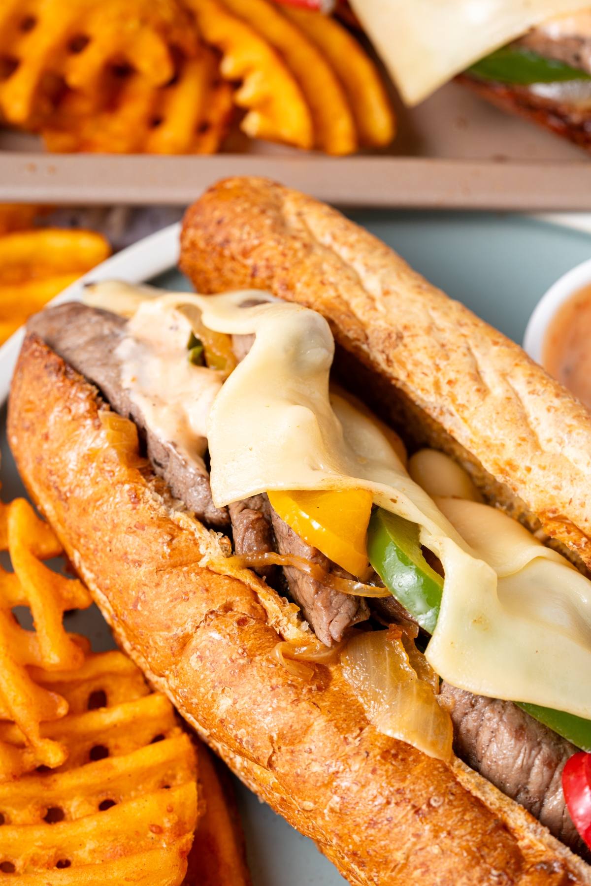A cheesesteak sandwich with melted cheese, peppers, and onions, served with waffle fries.