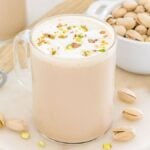 A mug of creamy pistachio latte topped with foam and chopped pistachios sits beside a bowl of whole pistachios.