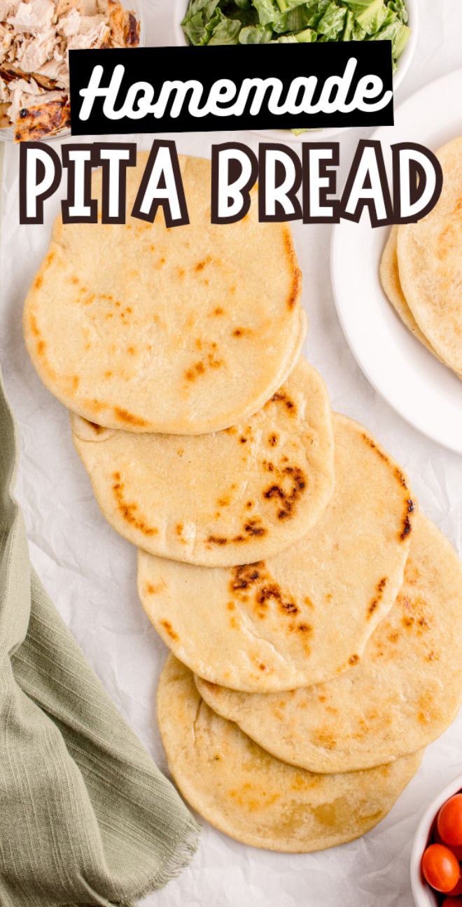 Five pieces of homemade pita bread are stacked on parchment paper, surrounded by fresh salads and flavorful toppings.