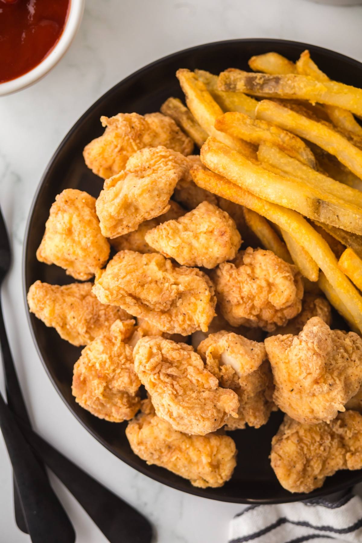 A plate of crispy chicken nuggets and golden French fries with a side of ketchup.