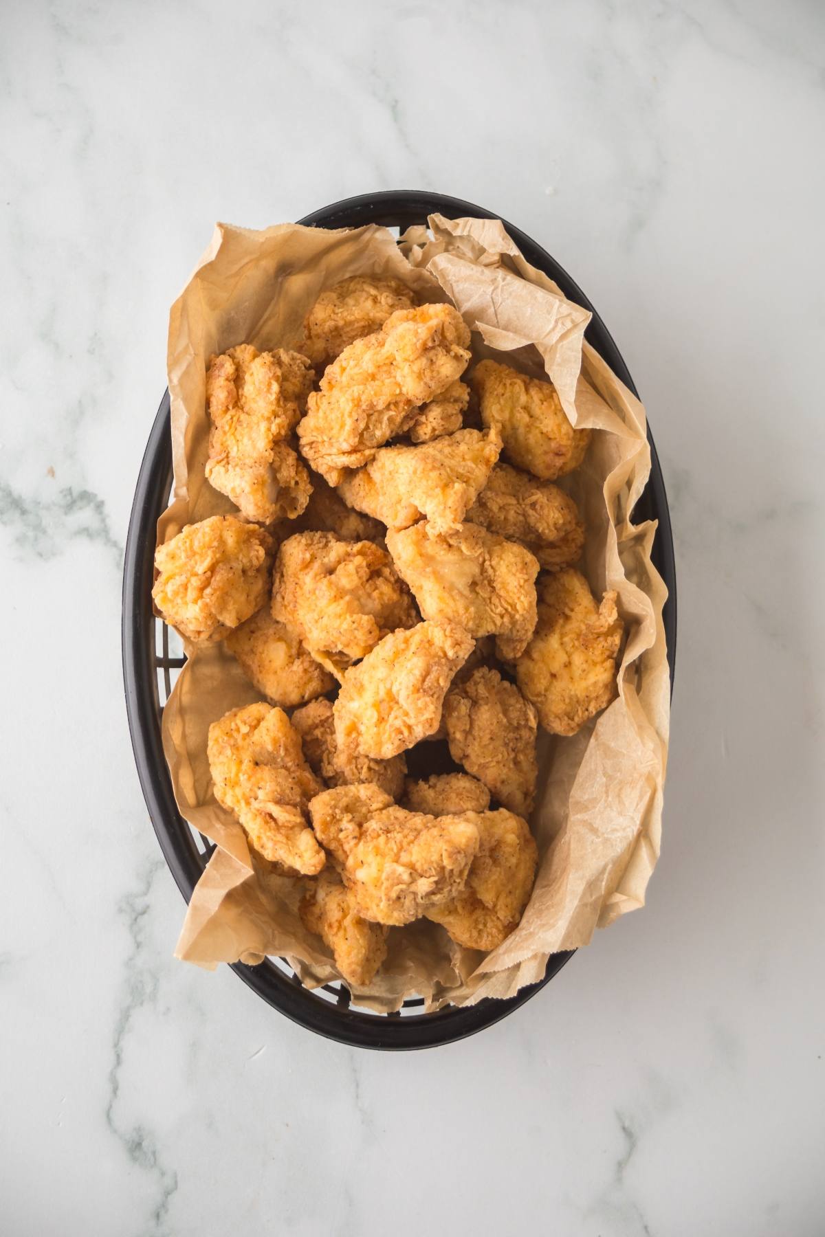 A basket lined with brown paper filled with crispy fried chicken pieces on a white surface.