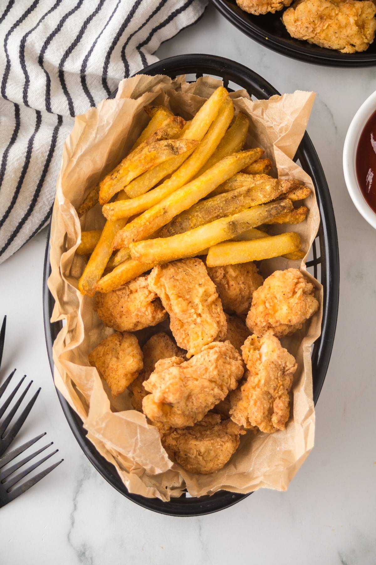 Basket of crispy chicken nuggets and golden French fries on parchment paper, with a striped napkin nearby.