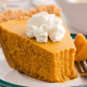 A slice of pumpkin chiffon pie with whipped cream on top sits on a plate with a fork.