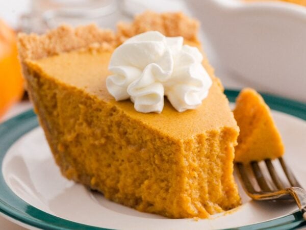 A slice of pumpkin chiffon pie with whipped cream on top sits on a plate with a fork.