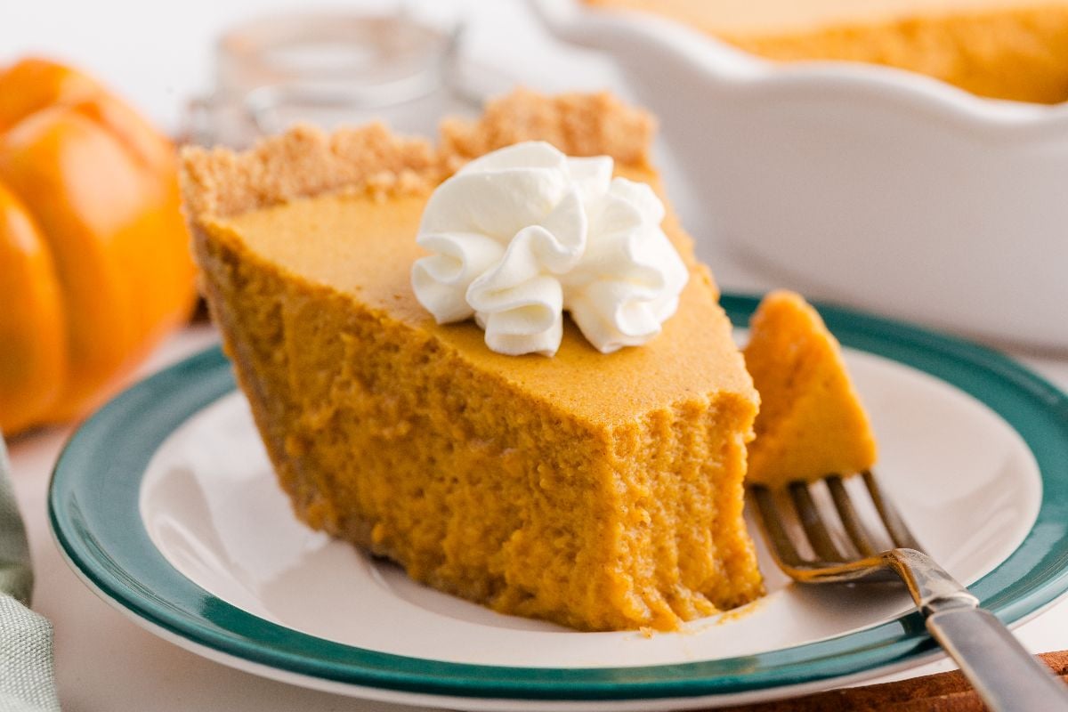 A slice of pumpkin chiffon pie topped with whipped cream rests on a plate with a fork.