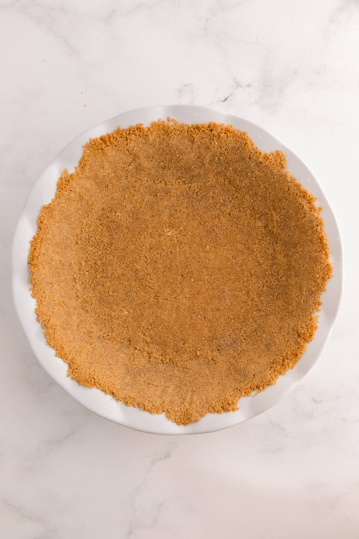A pie dish with an even layer of graham cracker crust pressed along the bottom and sides.