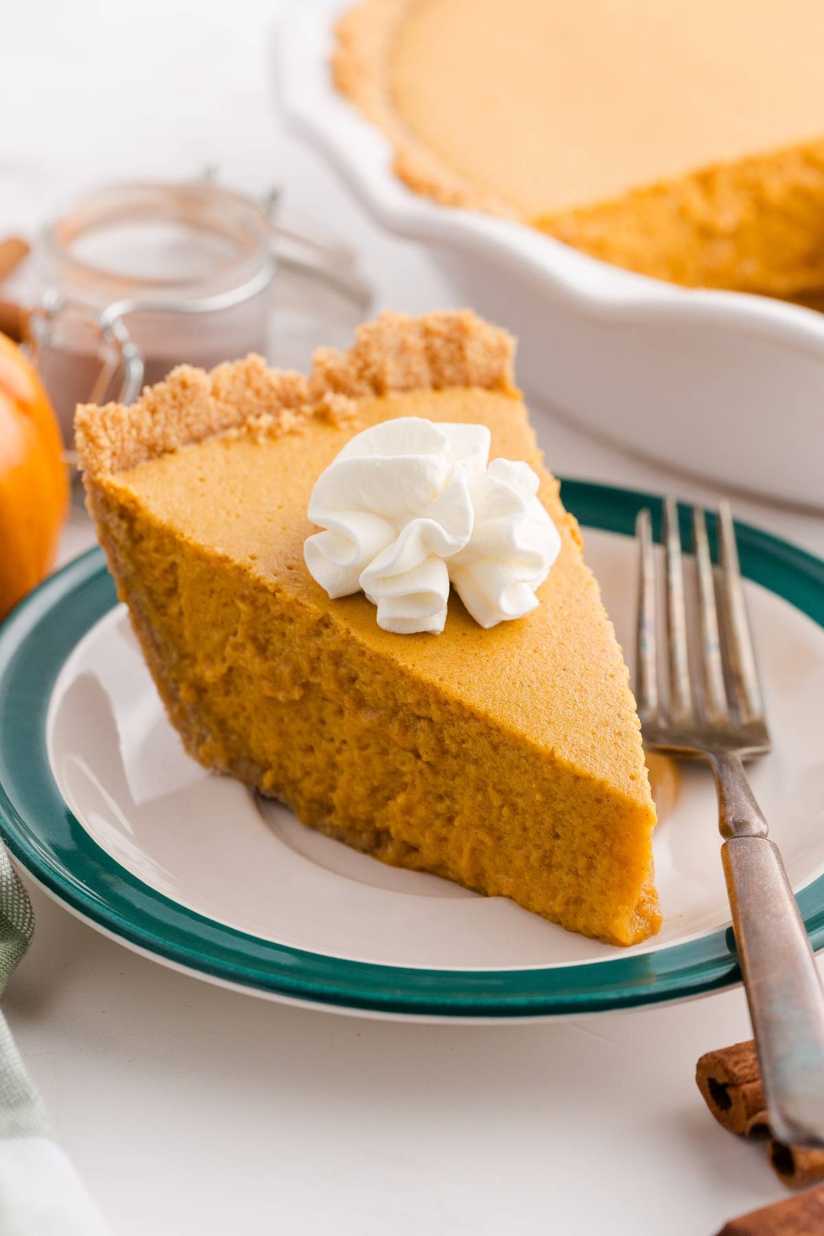 A slice of pumpkin pie with whipped cream on top, served on a plate with a fork.