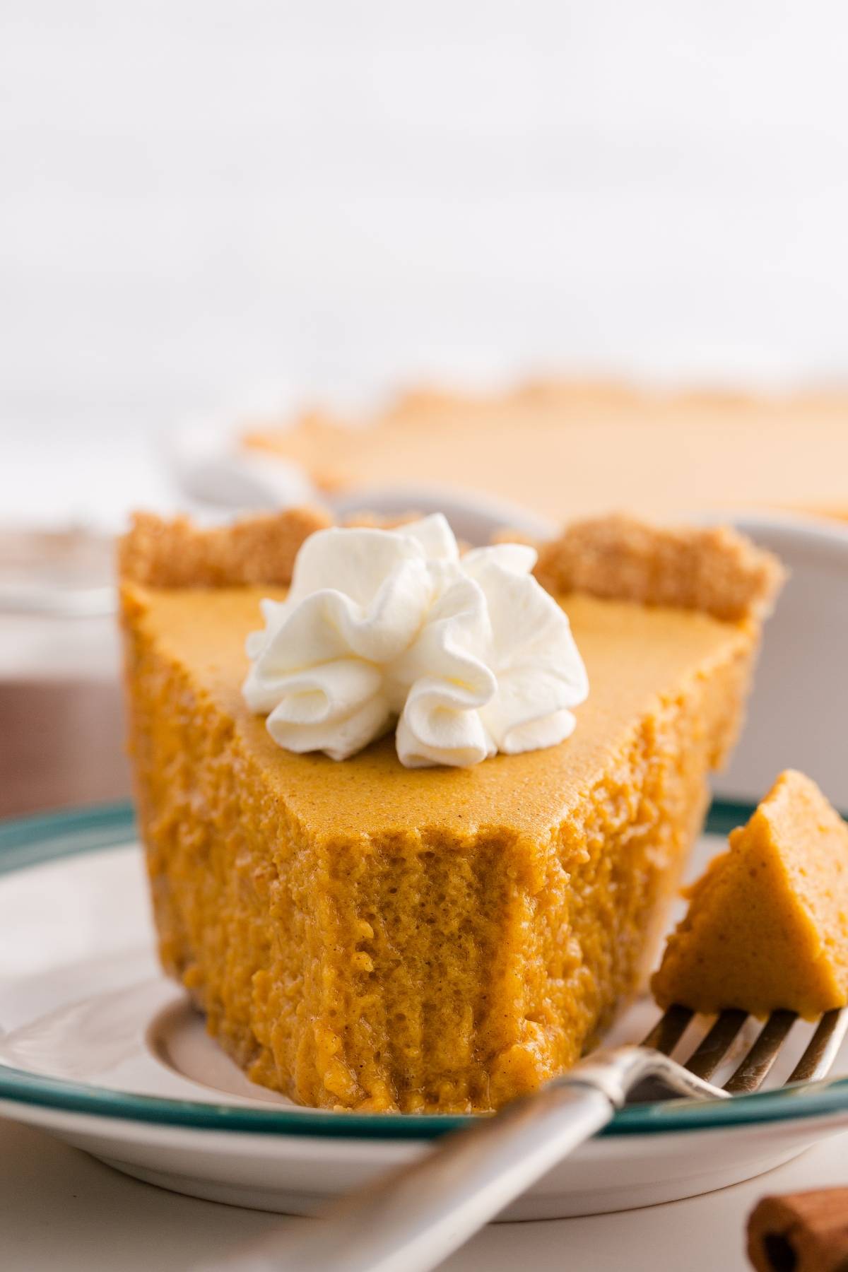 A slice of pumpkin pie with whipped cream on top, served on a plate with a forkful beside it.