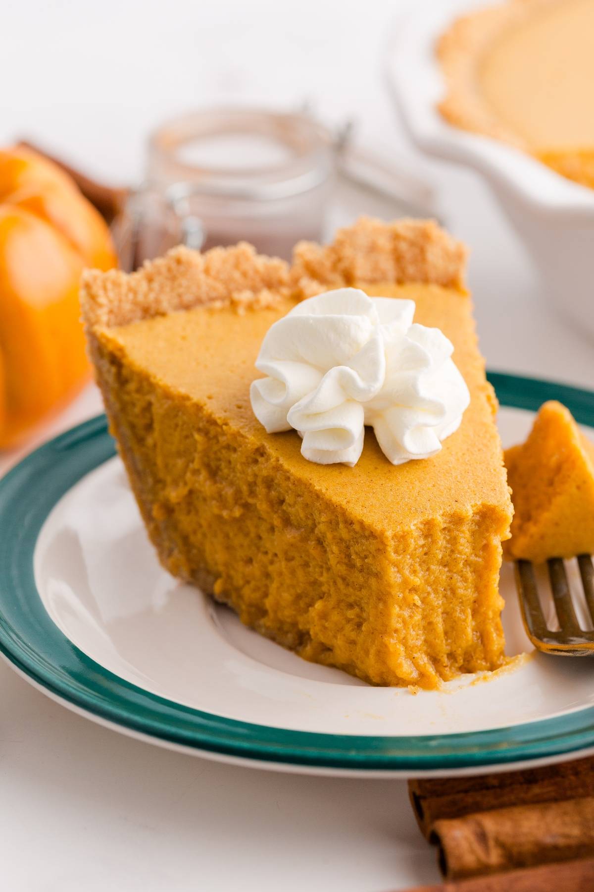 Slice of pumpkin pie with a dollop of whipped cream on top, served on a white plate with green rim.