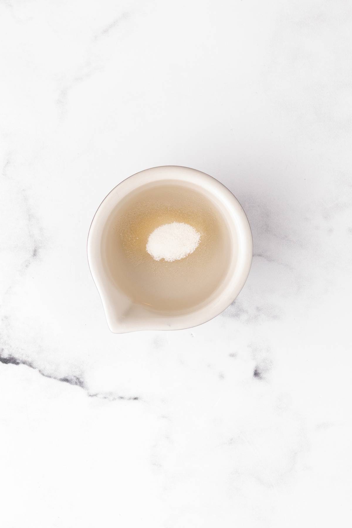 White powder in a small white bowl on a marble surface, viewed from above.