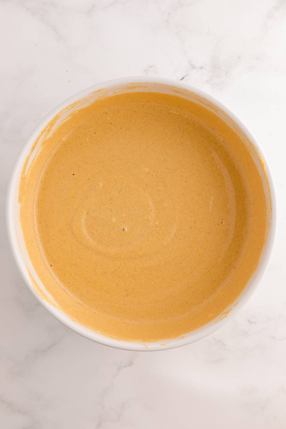 A bowl of smooth, light brown batter on a white marble surface.