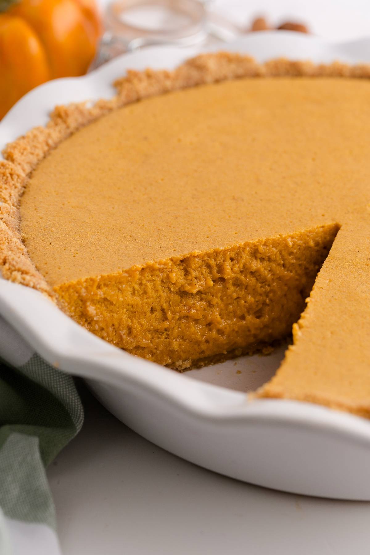 A pumpkin pie in a white dish with one slice missing, showing the creamy orange filling and crumbly crust.