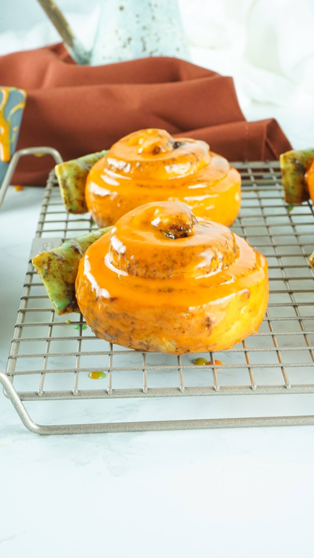 Glazed cinnamon rolls cooling on a wire rack with orange icing drizzled on top make the perfect pumpkin shaped dessert idea—try these pumpkins made from Pillsbury Grand Cinnamon Rolls for your next homemade pumpkin treat!.