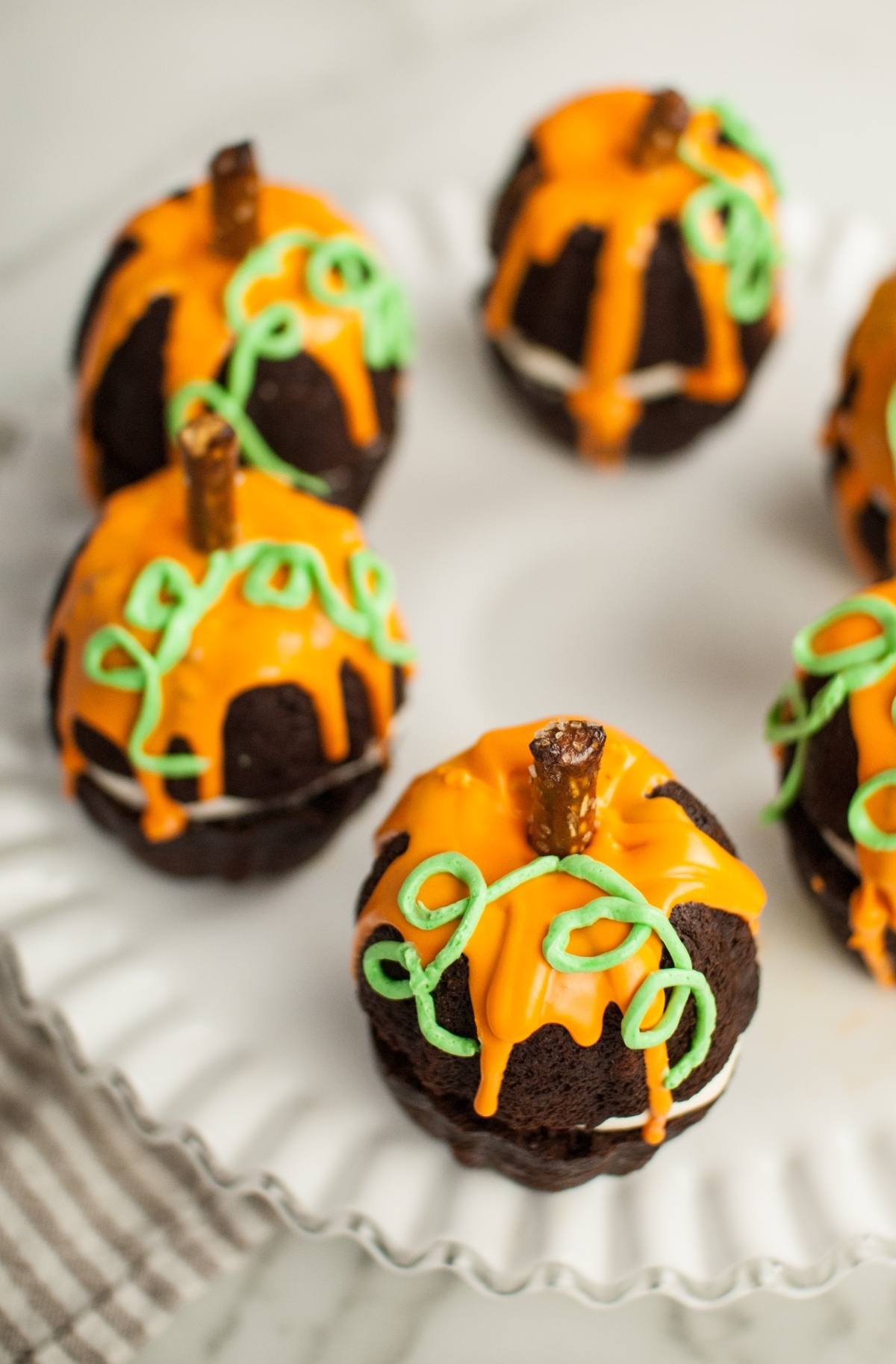 Chocolate cupcakes decorated as pumpkins with orange icing, green frosting vines, and pretzel stick stems—perfect as Halloween pumpkin cakes or a festive Thanksgiving or Halloween dessert.