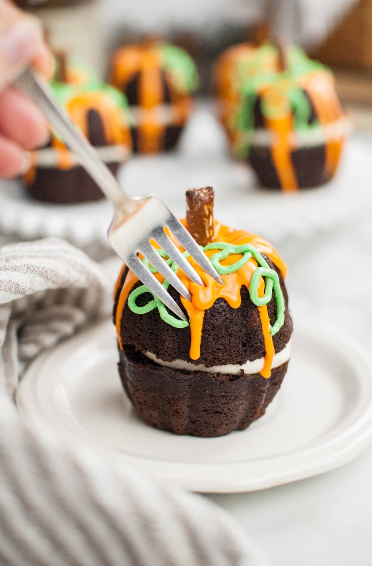A fork cuts into a pumpkin bundt cake with orange and green icing, shaped like a festive Halloween pumpkin cake, served on a white plate.