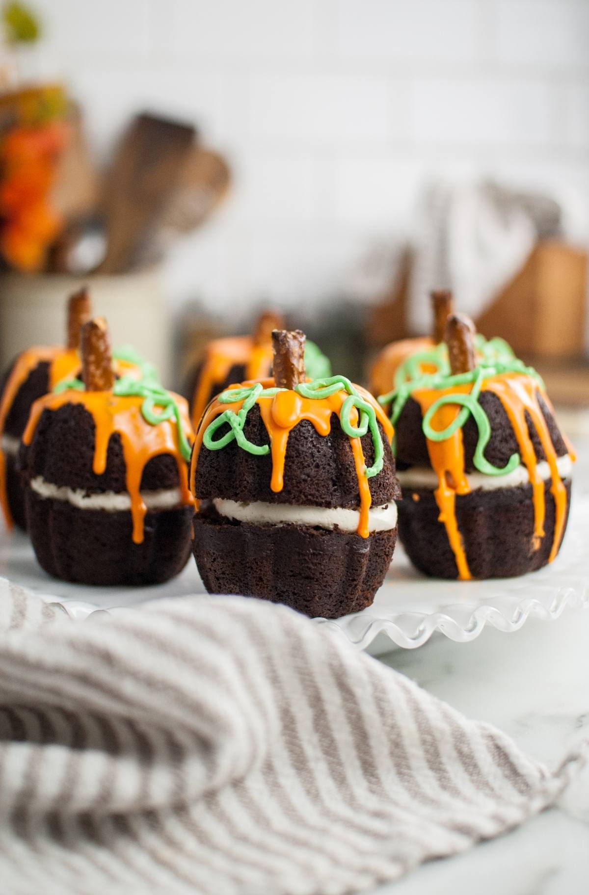 Chocolate pumpkin-shaped cakes with orange and green icing, topped with pretzel sticks, make the perfect Halloween pumpkin cakes for your next Thanksgiving or Halloween dessert display.