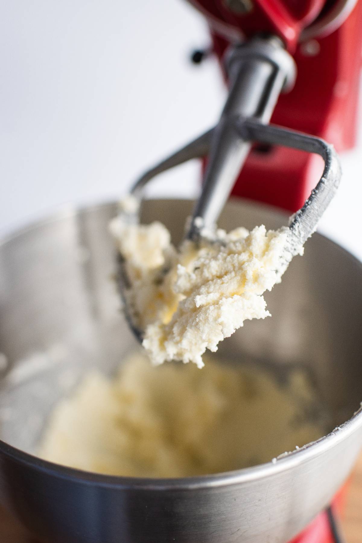Close-up of a stand mixer with creamed butter and sugar on the paddle attachment above the mixing bowl, ready for making classic thumbprint cookies or raspberry jam cookies.