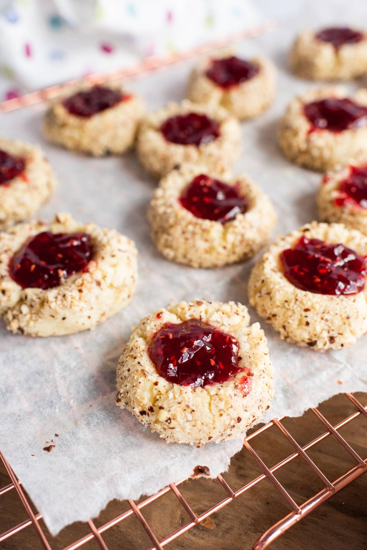 Classic hazelnut thumbprint cookies with jam cool on a wire rack, their red centers gleaming atop golden, buttery rounds.