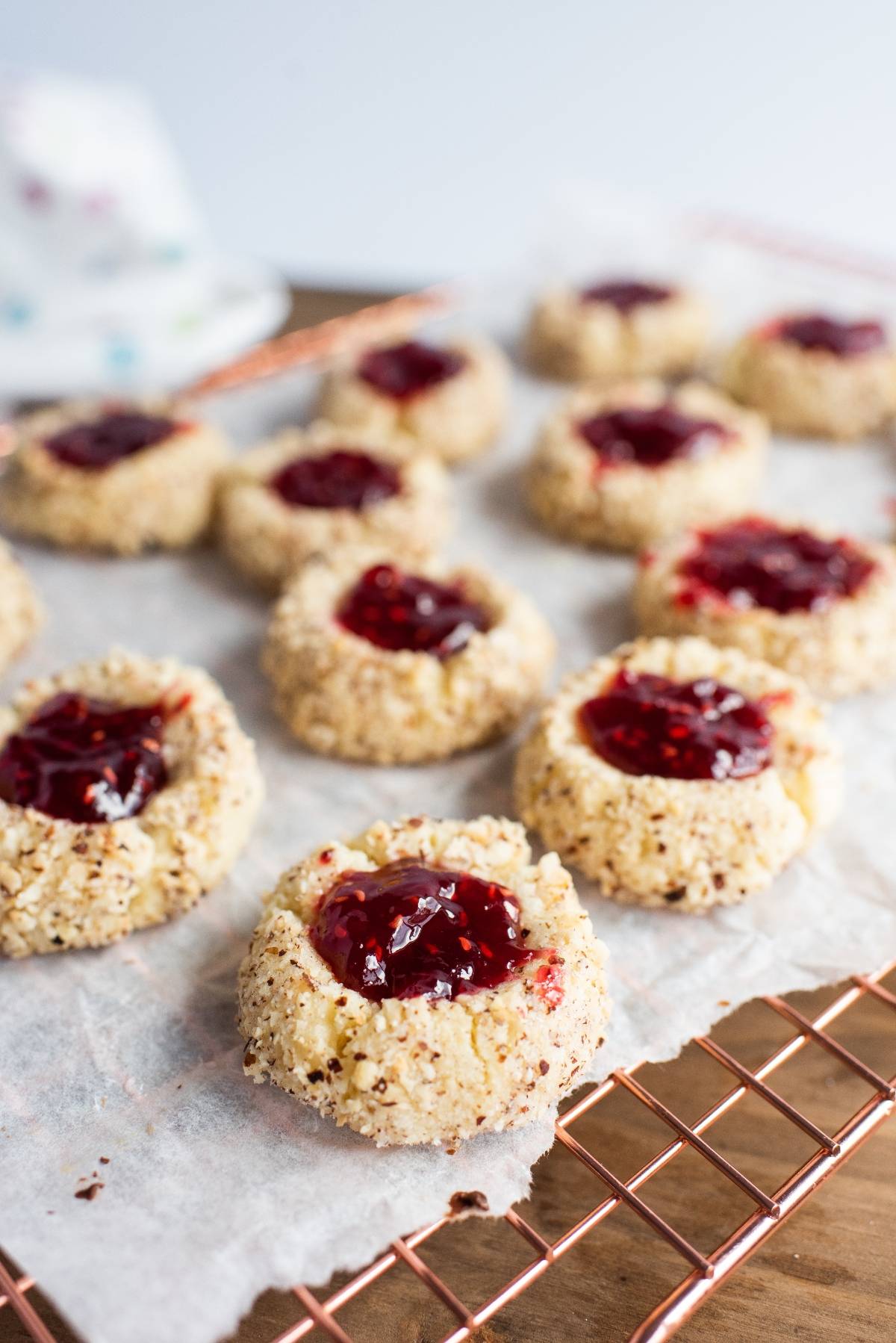 Raspberry hazelnut thumbprint cookies, filled with jam, rest on a parchment-lined cooling rack.