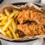 A basket of crispy spicy chicken tenders and golden French fries served on parchment paper.