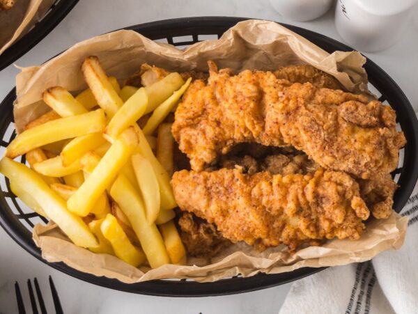 A basket of crispy spicy chicken tenders and golden French fries served on parchment paper.