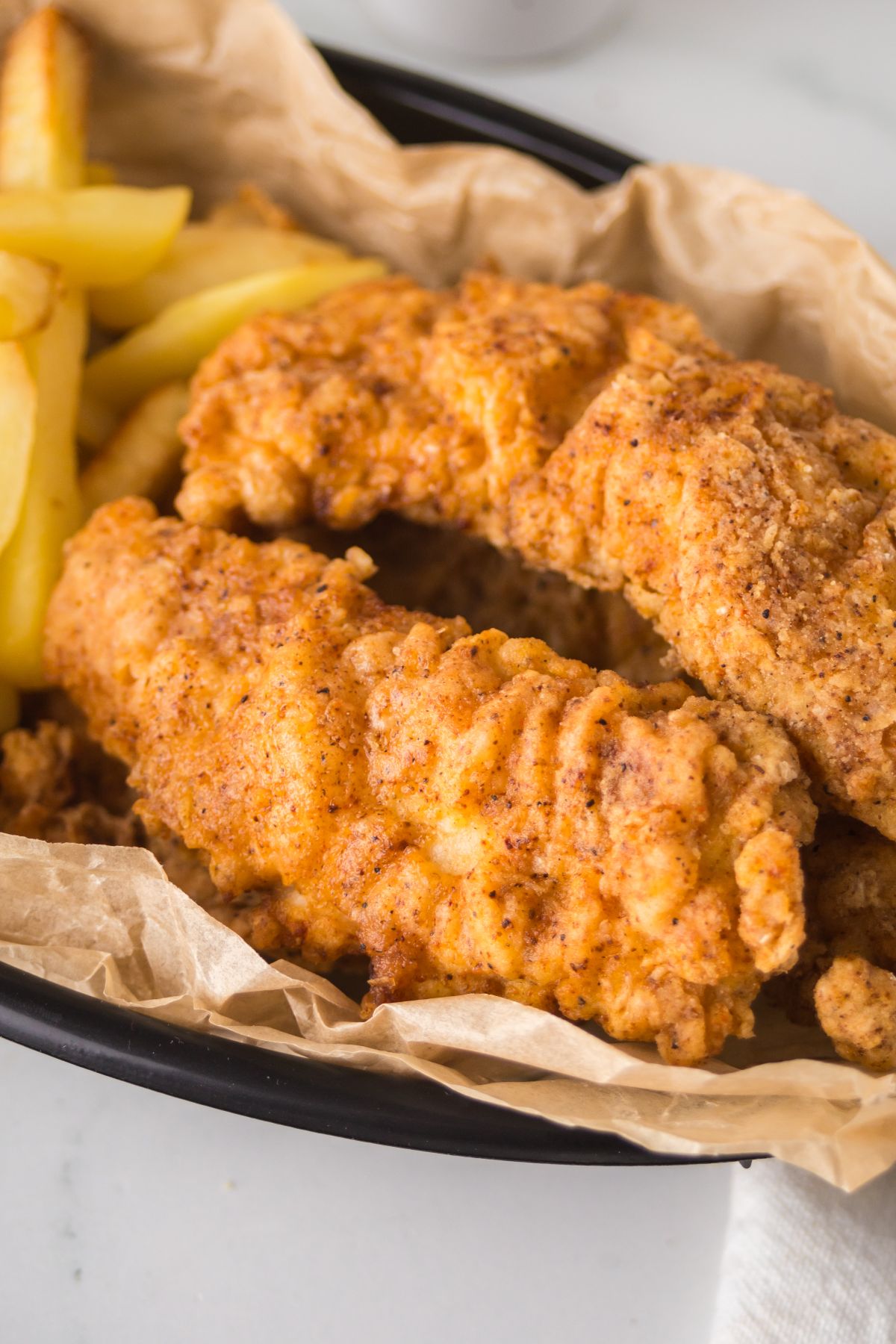 Spicy chicken tenders, crispy and golden, served with French fries in a basket lined with parchment paper.