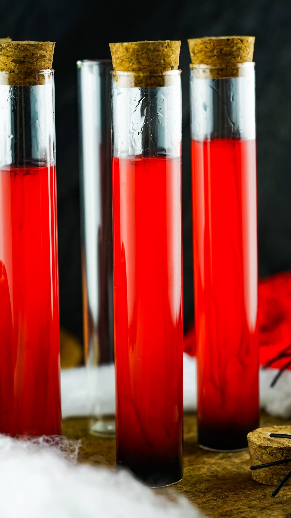Three tall glass tubes filled with red liquid and cork stoppers, one empty tube in the background—perfect as Vampire Kiss Halloween Vial Shooter or make ahead shots in a vial for your spooky celebration.