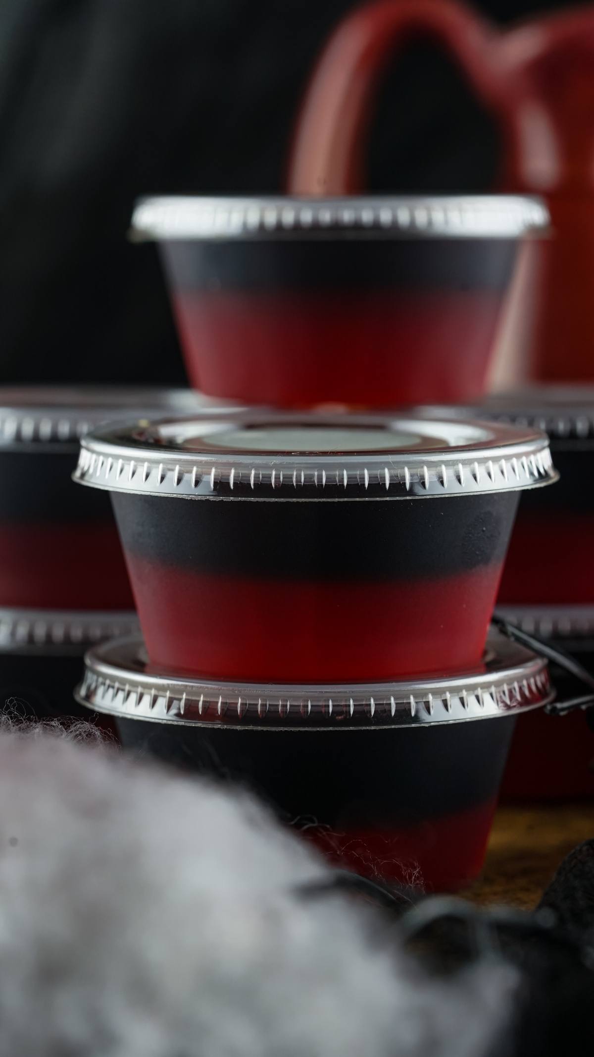 Stacked plastic containers filled with layered red and black gelatin, each sealed with a silver lid—perfect for Vampire Kiss Jello Shots or a spooky vampire blood jello shooter at your next Halloween party.