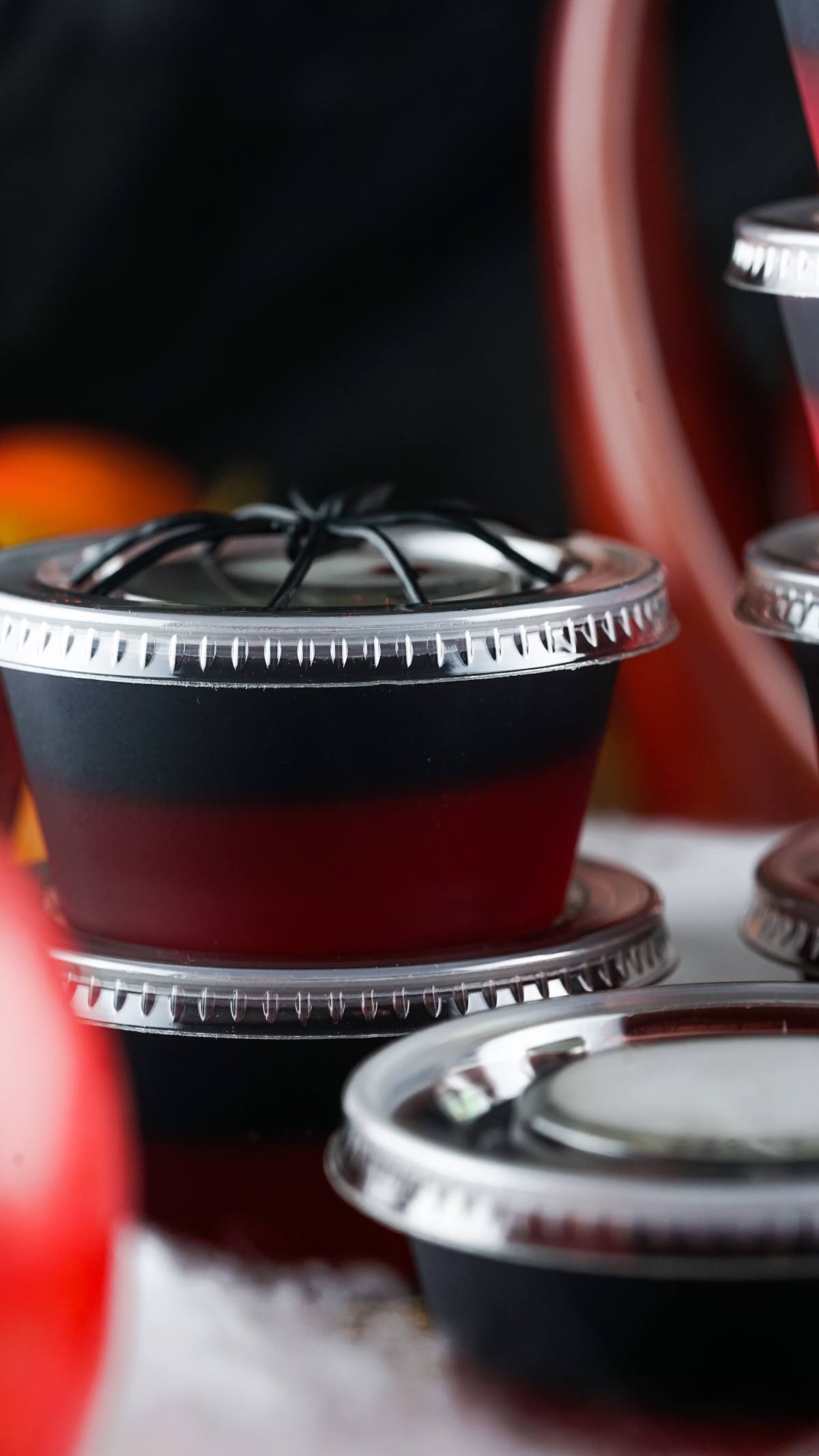 Two small plastic containers with lids, one stacked on top of the other, are perfect for serving a vampire blood jello shooter against a dark blurred background.