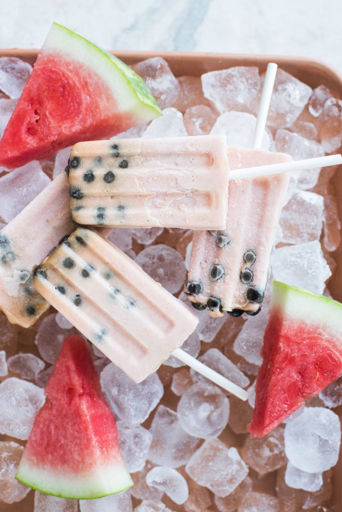 Watermelon boba popsicles with black seeds rest on ice, surrounded by fresh watermelon slices for a fun twist on classic summer treats.