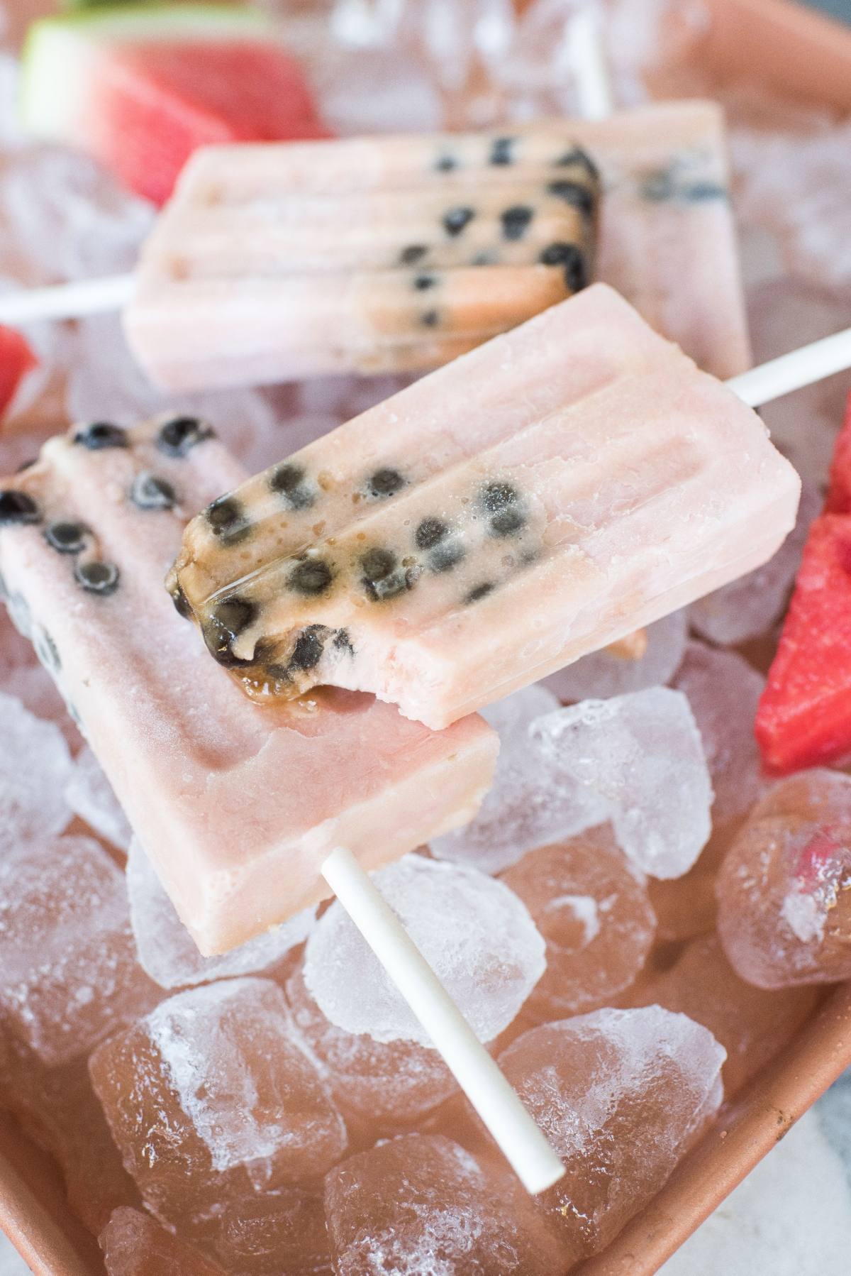 Watermelon boba popsicles with black seeds rest on ice cubes, surrounded by slices of watermelon.