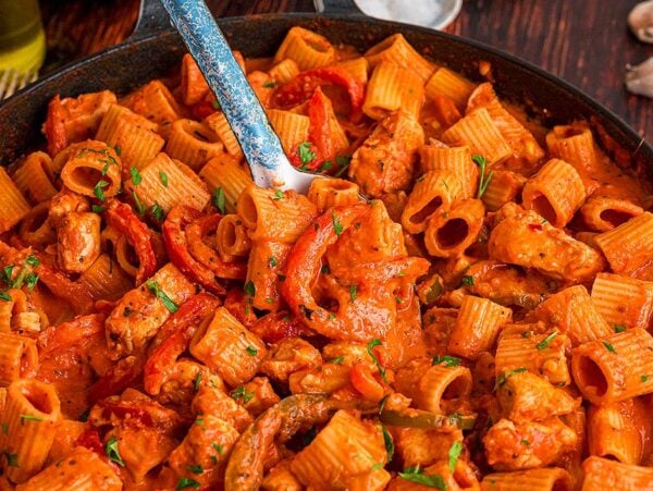 A skillet of chicken riggies—rigatoni pasta with chicken, red sauce, bell peppers, and herbs—served with a fork in the dish.