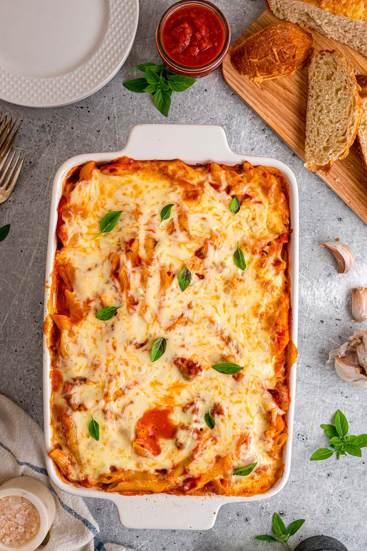 Baked mostaccioli pasta topped with melted cheese and basil leaves in a white dish.
