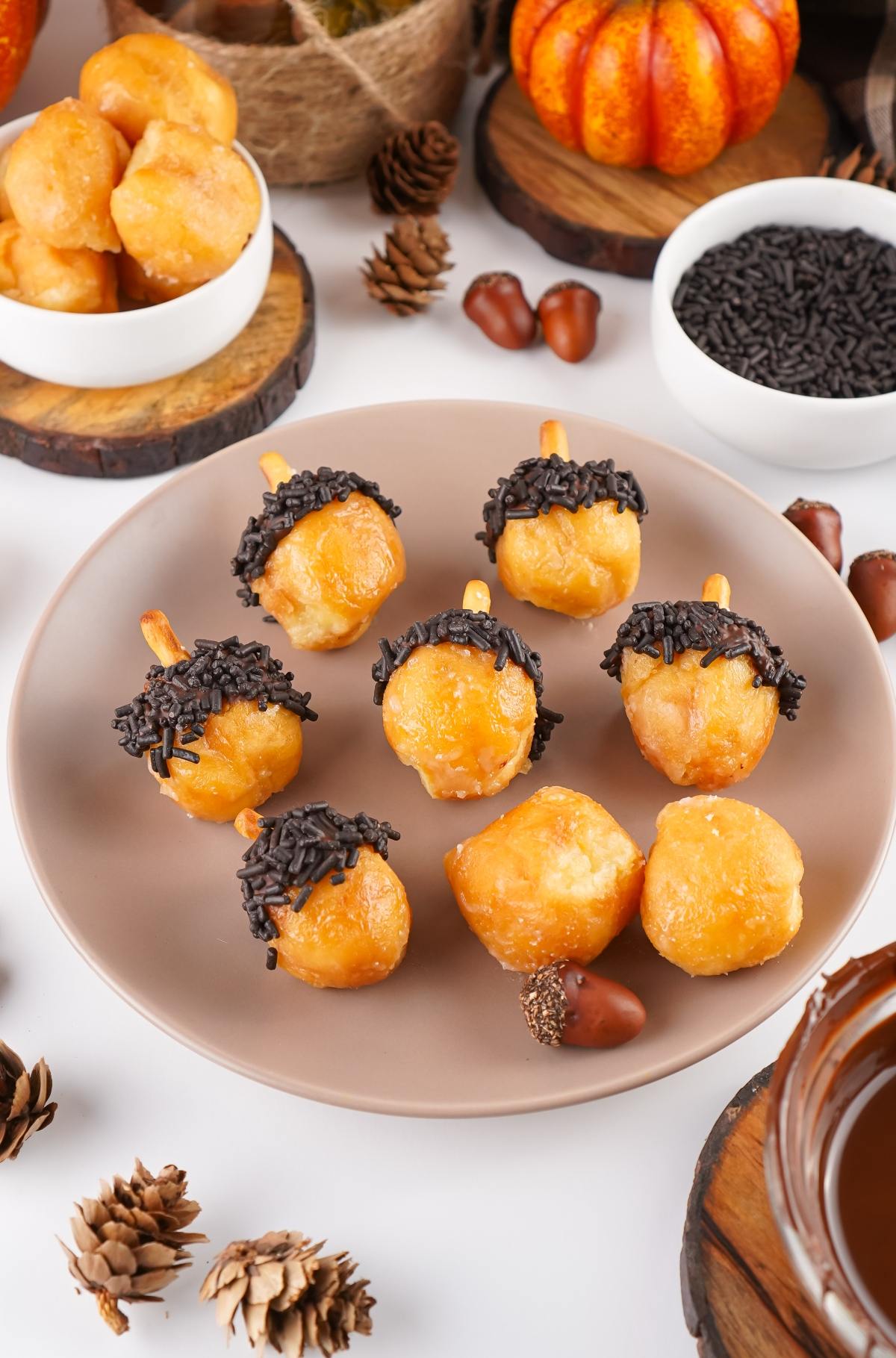Round pastries decorated with chocolate and sprinkles to look like acorns, arranged on a beige plate.
