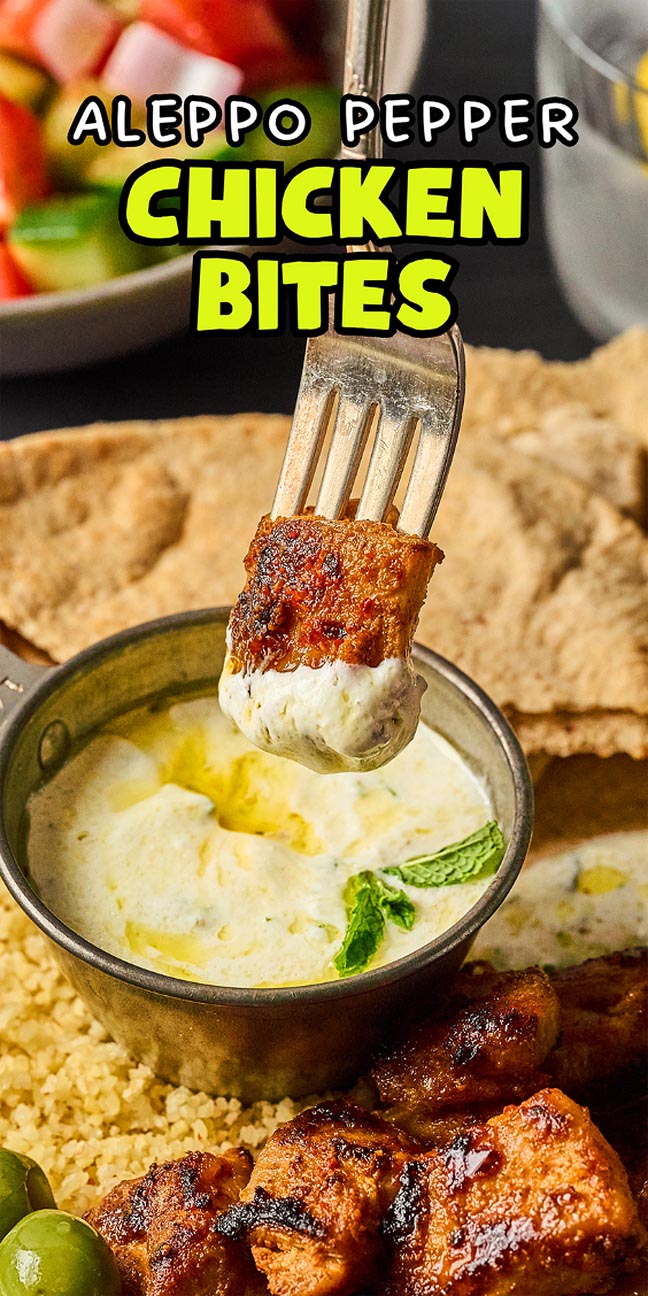 A fork holds a piece of Aleppo Pepper Chicken Bites dipped in white sauce, with pita and salad in the background.