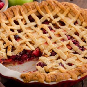 A lattice-topped apple cranberry pie with a slice missing, revealing a filling of mixed berries and apples.