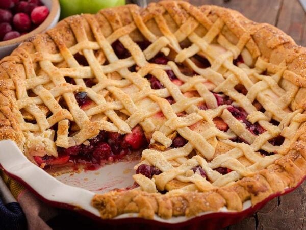 A lattice-topped apple cranberry pie with a slice missing, revealing a filling of mixed berries and apples.