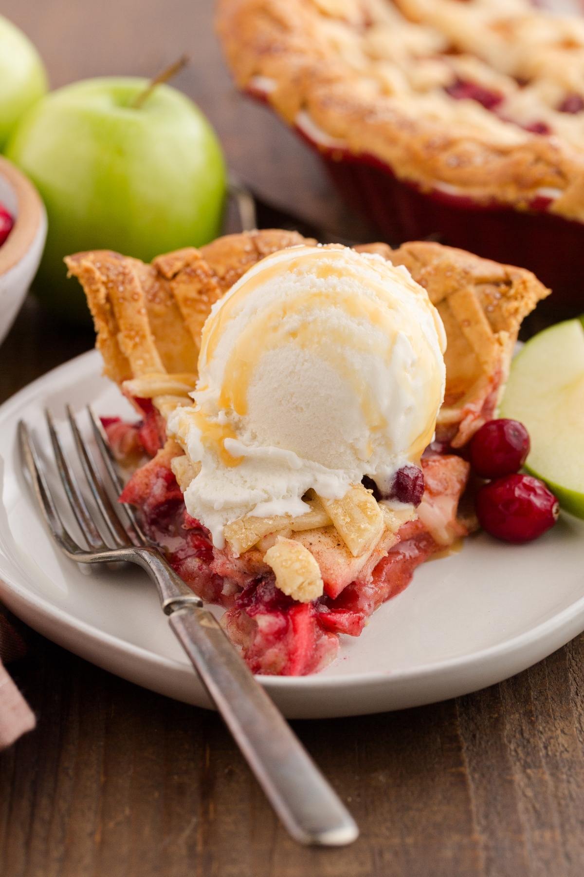 A slice of fruit pie topped with vanilla ice cream and caramel sauce on a plate with a fork.