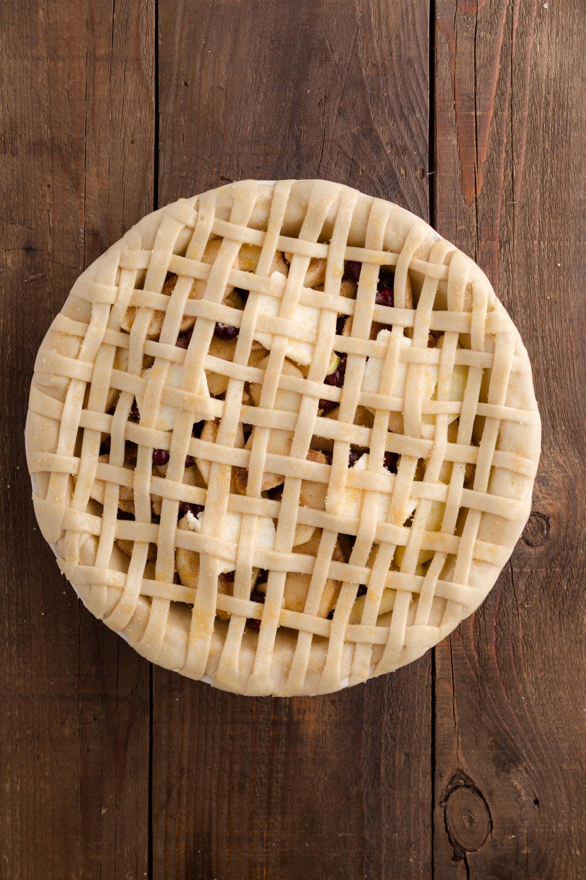 Unbaked pie with a lattice crust on a rustic wooden surface, viewed from above.