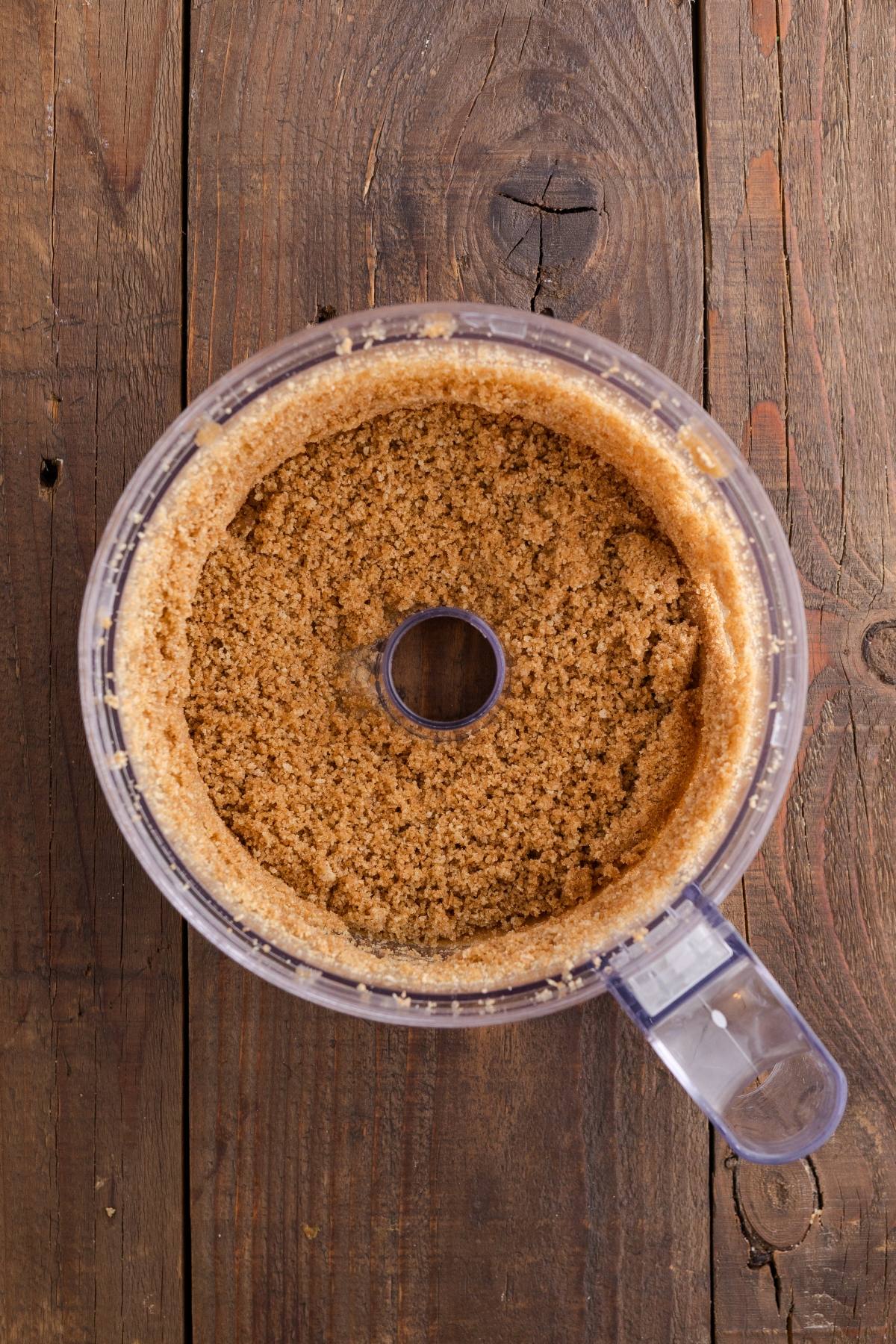Top view of brown sugar in a food processor bowl on a rustic wooden surface.