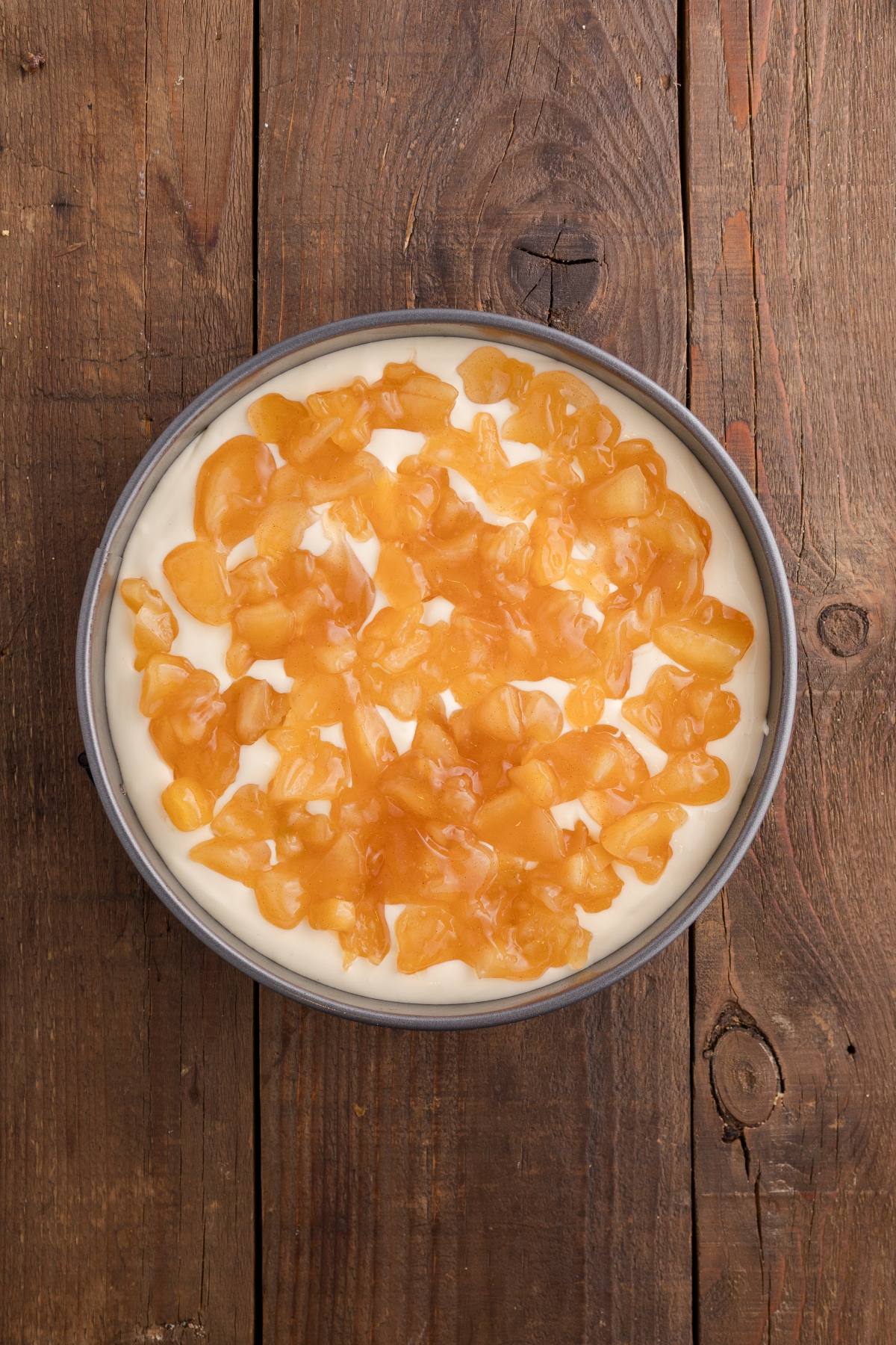 Round cheesecake topped with diced apple filling on a rustic wooden table.