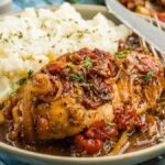 A plate of balsamic chicken smothered with gravy, tomatoes, and onions, served alongside mashed potatoes.