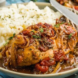 A plate of balsamic chicken smothered with gravy, tomatoes, and onions, served alongside mashed potatoes.