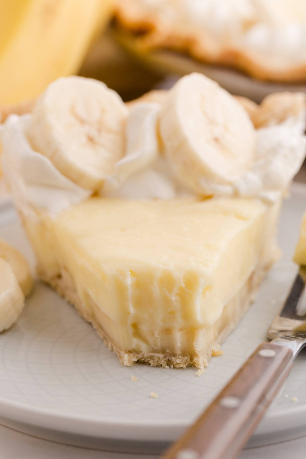 A slice of banana cream pie with whipped cream and banana slices on top, on a plate with a fork.