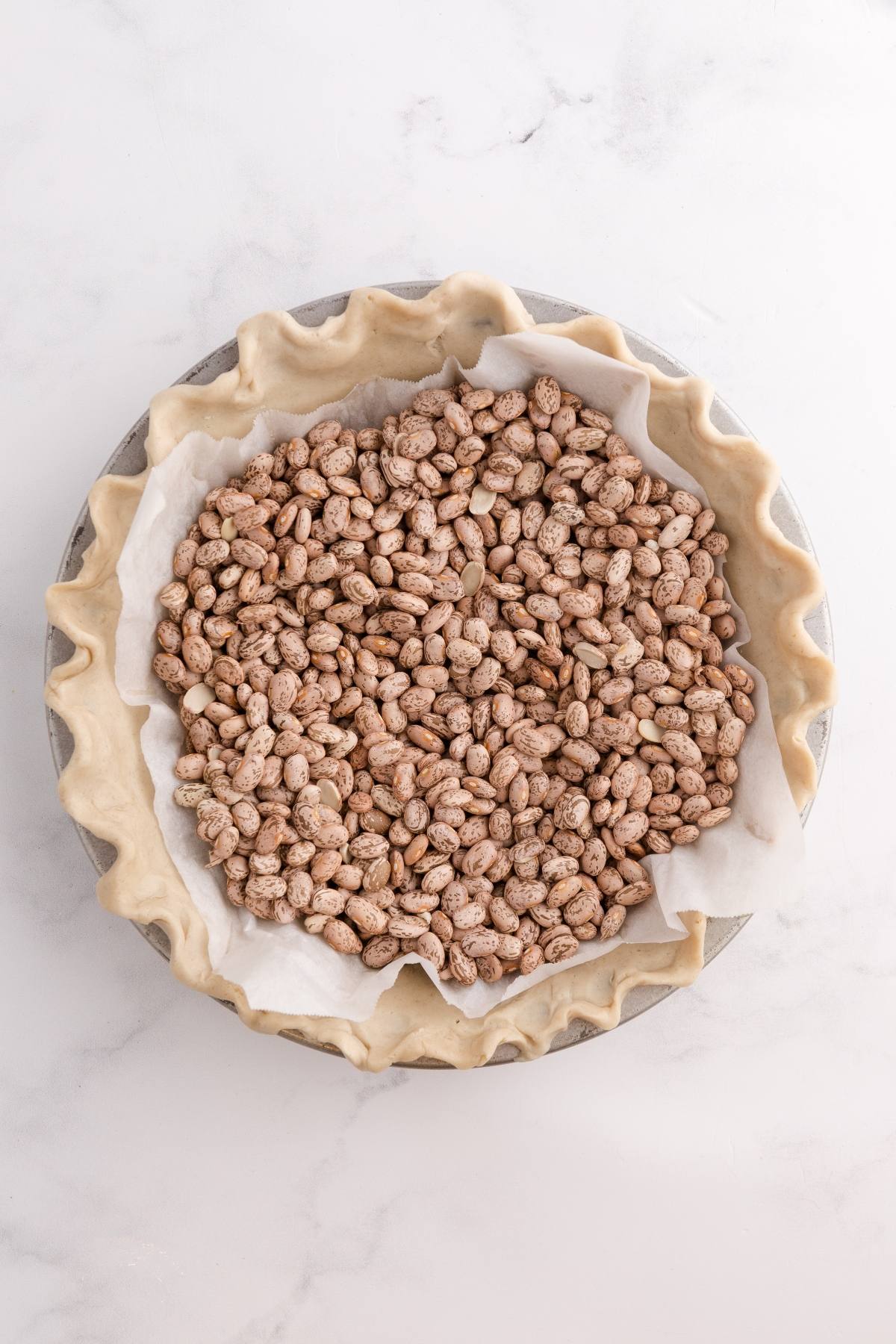 Unbaked pie crust lined with parchment paper and filled with dry beans for blind baking.