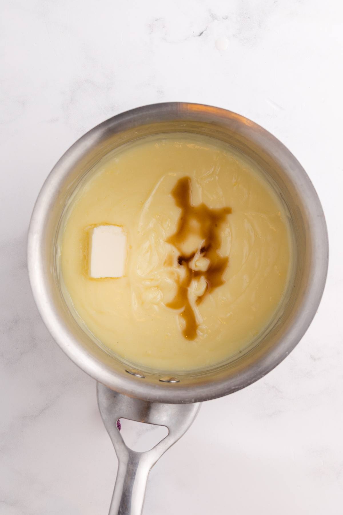 A saucepan with melted butter, vanilla, and sweetened condensed milk on a white surface.