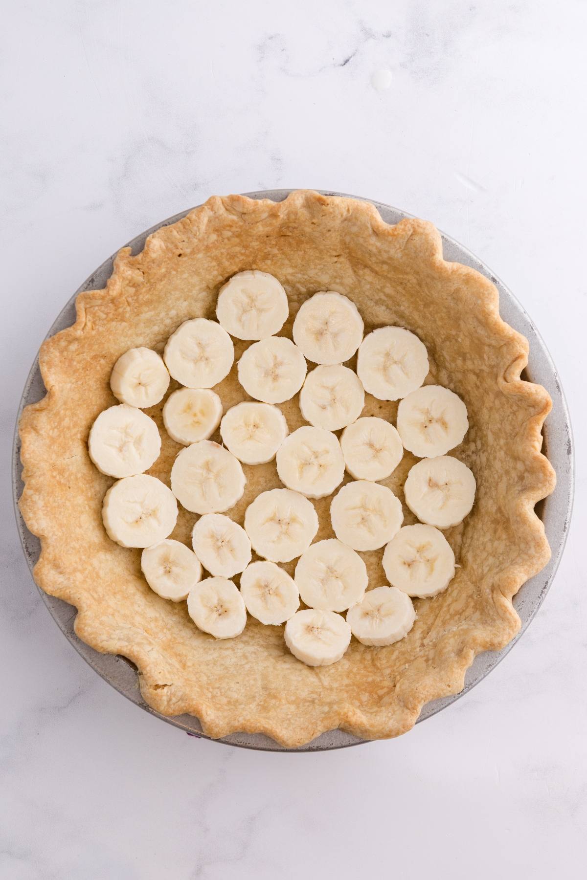 Sliced bananas arranged in a single layer on a baked pie crust in a round pie dish.