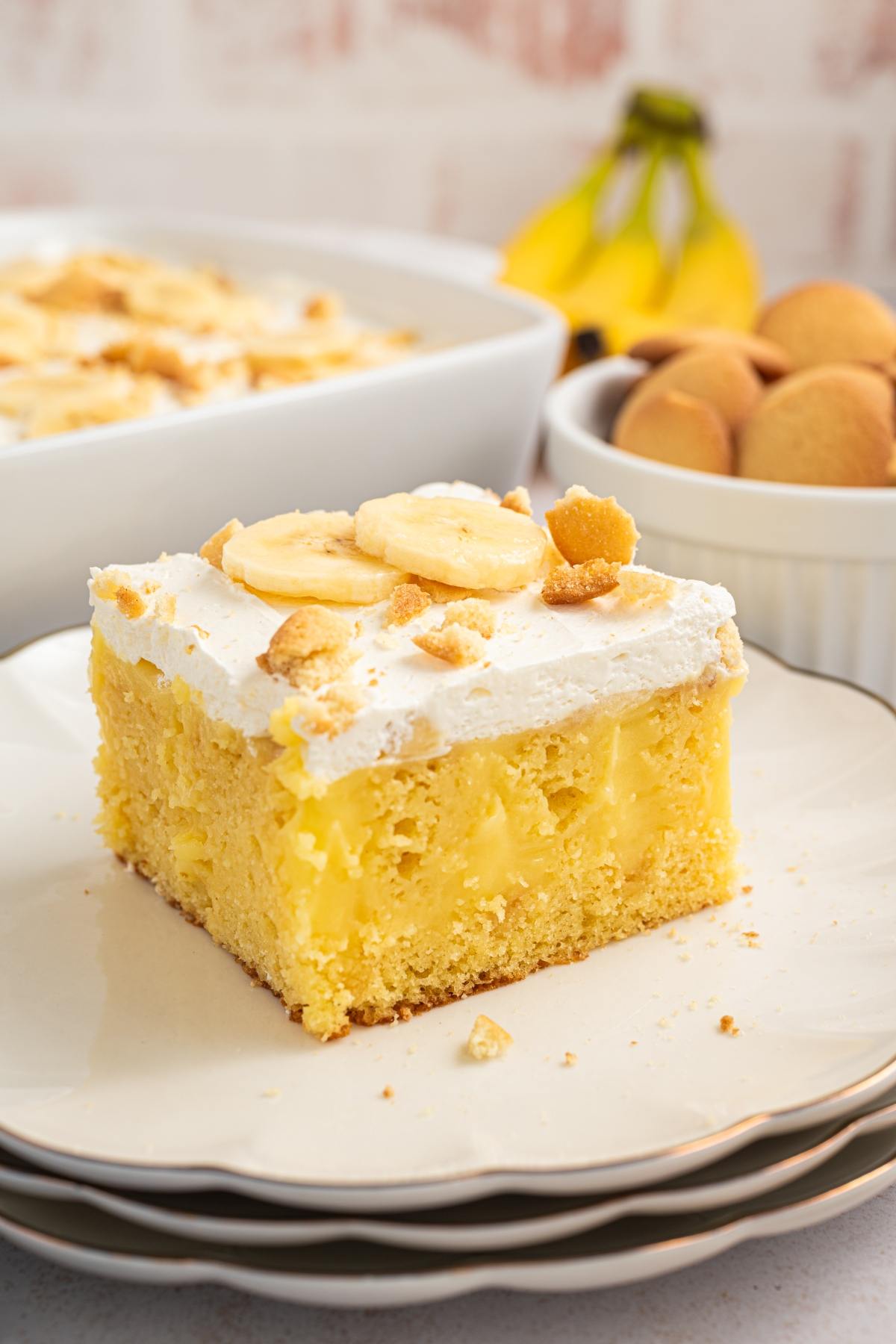 A slice of banana pudding cake topped with whipped cream, banana slices, and cookie crumbs on a plate.