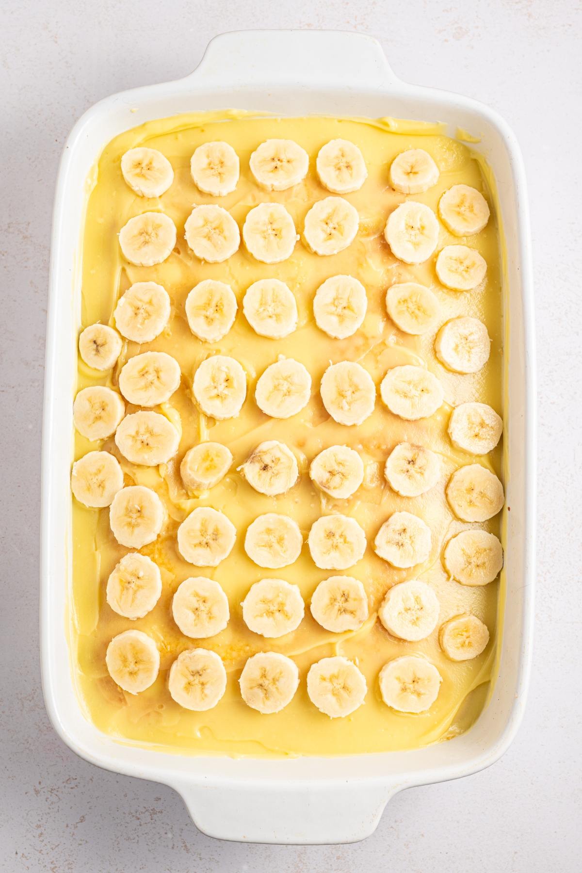 Rectangular dish with layers of pudding topped with evenly sliced banana rounds.